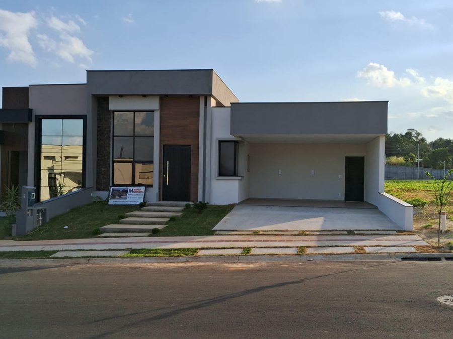 Residência térrea de fachada contemporânea com obra retomada e concluída, ainda com a placa de responsabilidade técnica da engenharia no terreno
