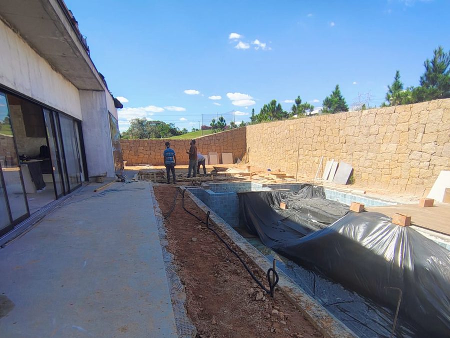 Ampliação de área externa com piscina executada e vala aberta para instalações, ao lado da varanda de residência em condomínio